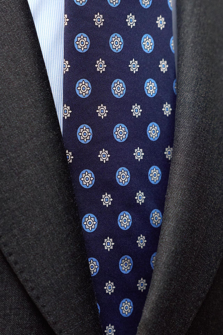Gravata Napoli em seda azul marinho com estampado geométrico circular em tons de café com leite.